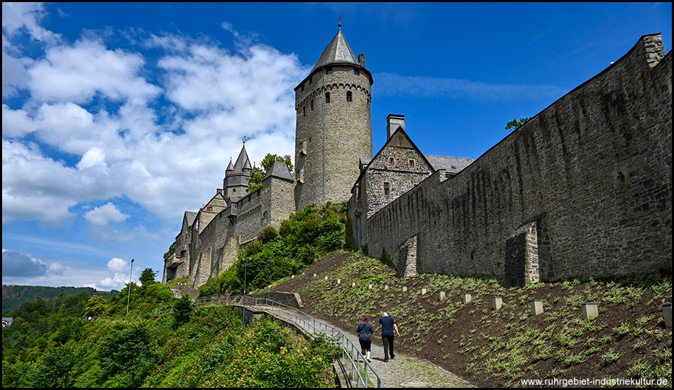 Eine Burg auf einem Berg mit Ringmauer, Palas und Bergfried vor blauem Himmel mit dekorativen Wolken