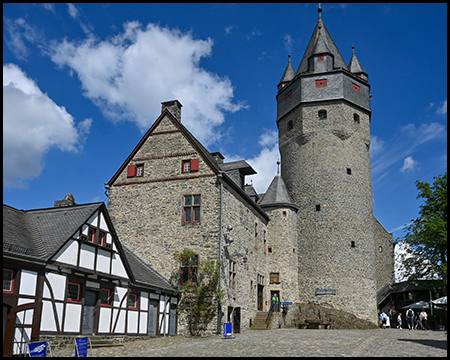 Ein Burghof mit Fachwerkhaus, großem Steingebäude und einem Turm mit Schieferdach