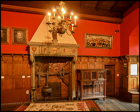 Ein Kamin in einem großen Raum einer Burg mit Wandvertäfelung aus Holz und roter Wand