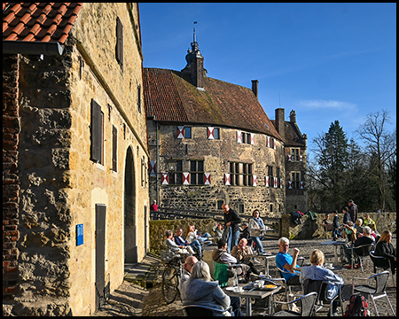 Burg Vischering und Vorburg mit Tischen und Stühlen, an denen Menschen sitzen und Getränke oder Kuchen verzehren
