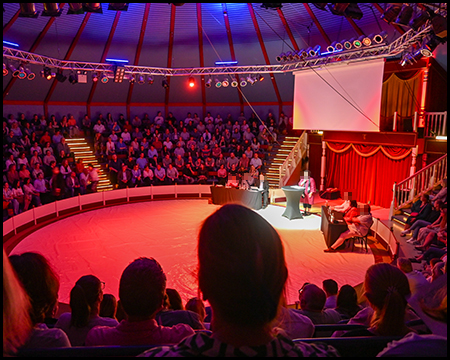 Im Innern eines festen Zirkuszeltes mit Blick vom oberen Rang auf die Zuschauer und die Manege