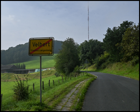 Ortsausgangsschild von Velbert in einer Tal-Landschaft. Im Hintergrund ist ein Sendemast zu sehen