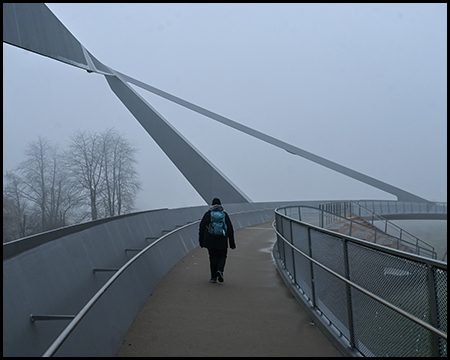 Eine Person auf einer Fußgängerbrücke mit einem geneigten Pylon. Die Szeen ist im Nebel.