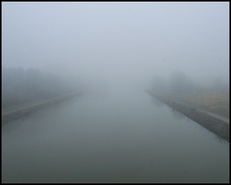 Blick von einer Brücke auf einen Kanal. Die ganze Szene ist im Nebel