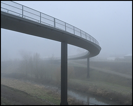 Ein Teil einer Brücke über einen Fluss im Nebel. Die Brücke macht eine langgezogene Kurve nach links.