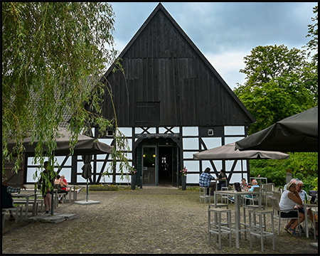 Ein Fachwerkhaus von der Giebelseite gesehen, davor Tische und Stühle eines Cafés auf einem Hof