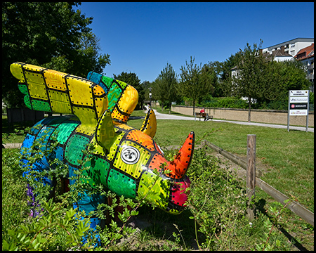 Ein bunt bemaltes Nashorn mit Flügeln als Kunstobjekt in einem Park