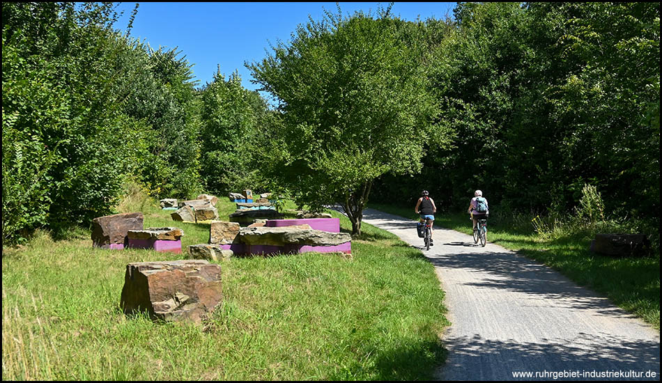 Radfahrer auf einem Weg neben einem Kunstwerk aus Steinen und 3D-Kunststoffdruck