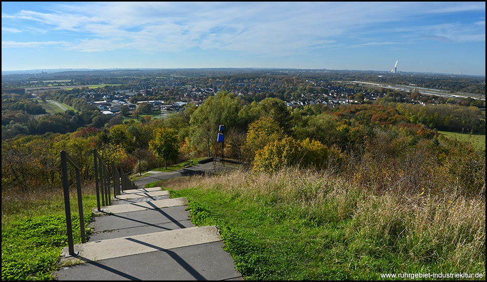 Treppe an einem Berghang. Weiter unten herbstliche Umgebung mit Siedlung und vielen Bäumen