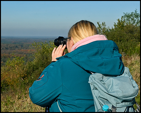 Eine Frau fotografiert von einem Berg eine herbstlich gefärbte Landschaft