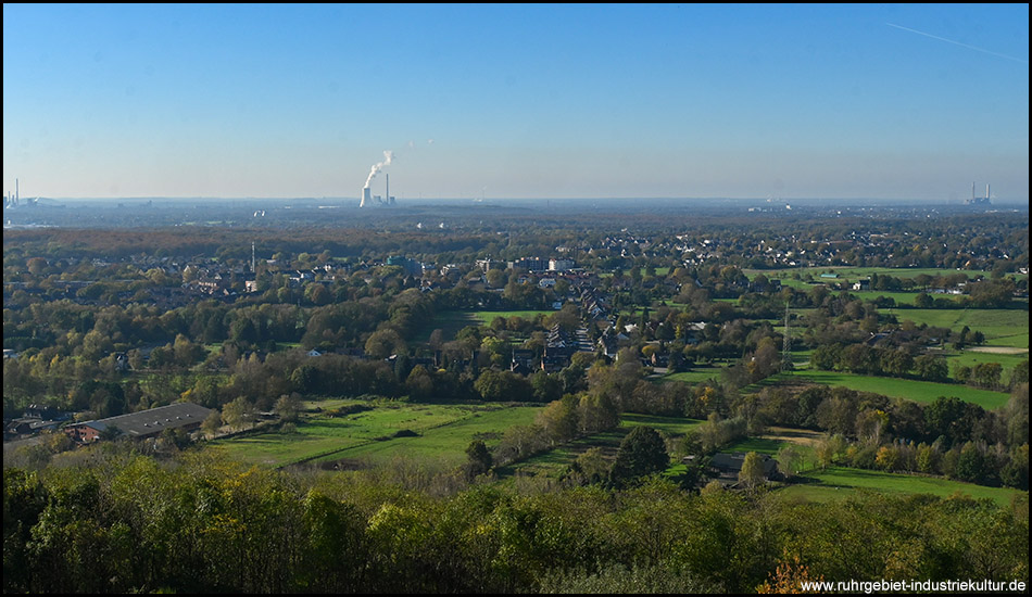 Landschaft unterhalb eines Berges mit vielen Siedlungen, Wäldern, Hecken und Bäumen. Im Hintergrund ist ein Kraftwerk mit dampfendem Kühlturm zu sehen