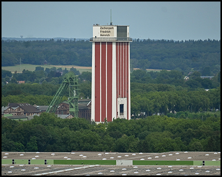 rot-weißer kubischer Förderturm und ein grünes Fördergerüst einer Zeche