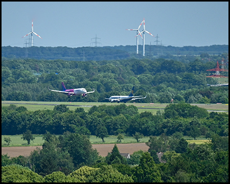 Ein landendes Flugzeug fliegt vor einem vor der Startbahn stehenden vorbei. Blick von der Halde Schleswig auf den tiefer gelegenen Dortmunder Flughafen