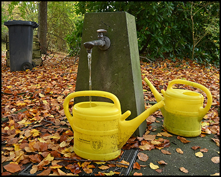 Zapfstelle auf einem Friedhof mit zwei gelben Gießkannen