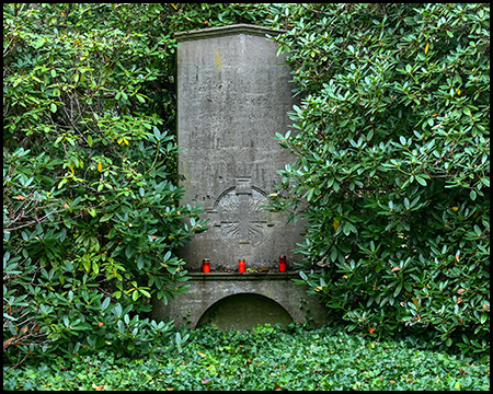 Ein Denkmal im Grün mit einigen Grabkerzen