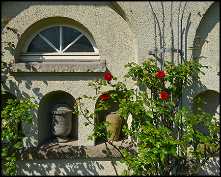 Urnen in einer Mauernische, daneben Rosenstöcke
