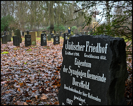 Ein Gräberfeld mit jüdischen Grabsteinen im Herbst. Vorne eine Inschrift, die diesen als Jüdischen Friedhof bezeichnet.