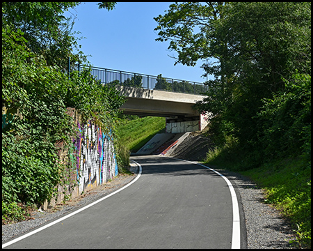 Radweg auf alter Bahntrasse mit Stützmauer und einer Straßenbrücke