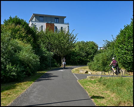 Radweg zwischen Wohnhäusern. Zwei Radfahrende queren auf einem Zuweg von der Seite.