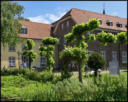 Ein Garten mit Bäumen, dahinter Gebäude von Kloster Saarn