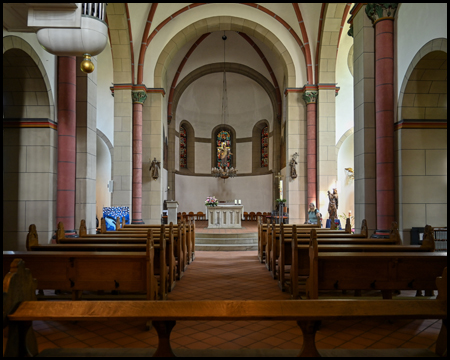 Im Innern einer romanischen Kirche mit Sitzbänken und Blick zum Altarraum