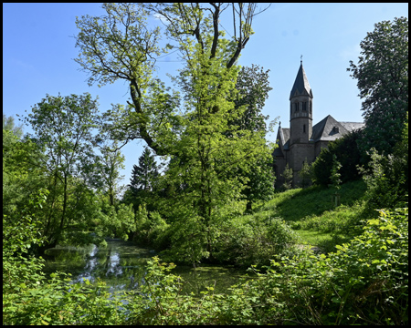 Eine grüne Teichlandschaft mit Bäumen und einem erhöht stehenden Gebäude mit Turm, dem Kloster Saarn