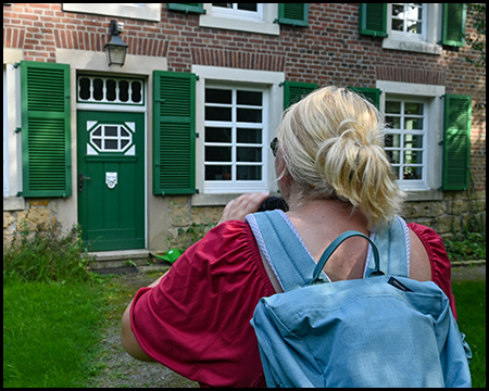 Eine Frau fotografiert eine Gebäudefassade mit schöner Haustür und Fenstern mit grünen Läden