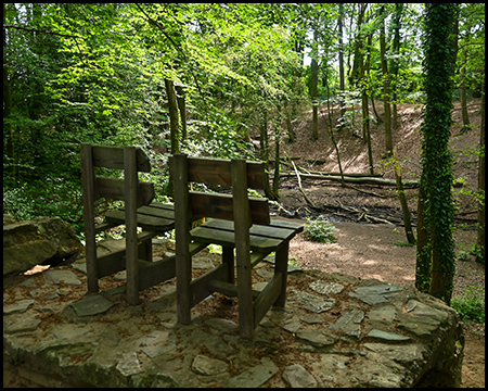 Zwei Stühle auf einer steinernen Plattform über einem bewaldeten Bachtal