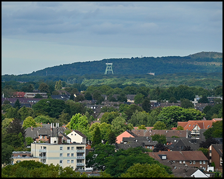 Blick aus der Höhe auf Häuser einer Siedlung. Im Hintergrund ein Fördergerüst vor einer Bergehalde