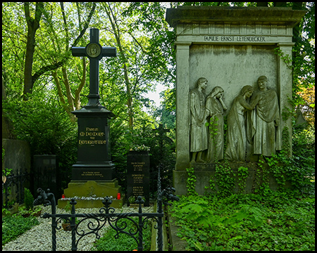 Zwei Grabstätten, eines mit einem steinernen Kreuz, eines mit einem Reliefbild als Grabstein