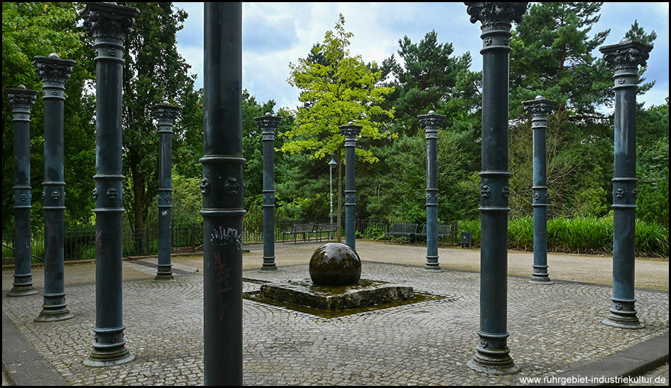 Ein Platz mit einem Kugelbrunnen und ringsherum stehenden Stahlsäulen