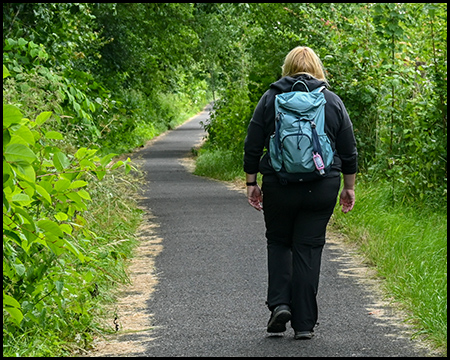 Eine Frau spaziert mit Rucksack auf einem asphaltierten Weg