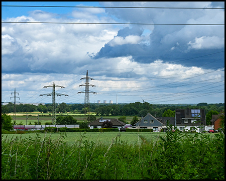 Aussicht auf eine flache Landschaft mit einer Siedlung, Felder und eine Hochspannungsleitung unter dramatischen Wolken