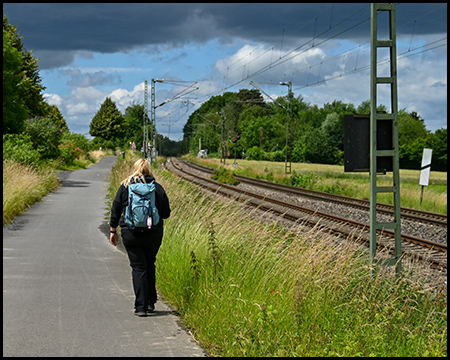 Eine Frau spaziert auf einem asphaltierten Weg parallel zu einer Bahnstrecke