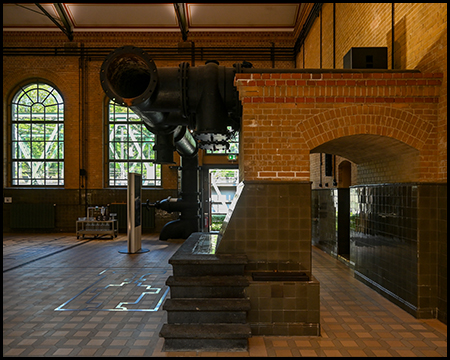 Im Innern einer Halle mit hohen Rundbogenfenstern, Stützmauern und Rohren