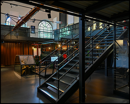 Treppen in einer Halle auf eine Empore. Darunter Exponate eines Museums