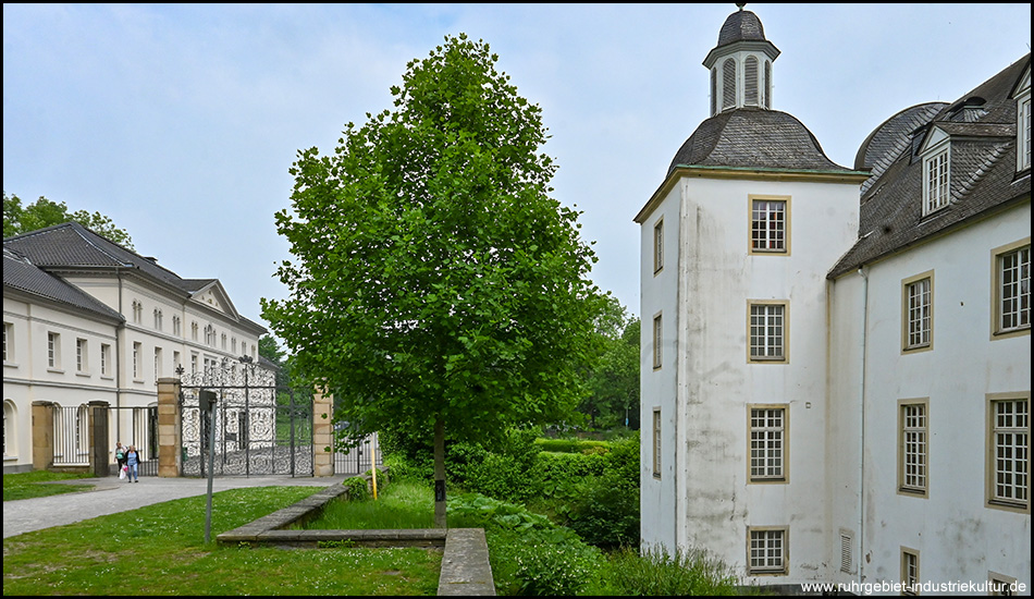 Breites Bild mit einem Wasserschloss und einem daneben stehenden Gebäude in einer Parkanlage