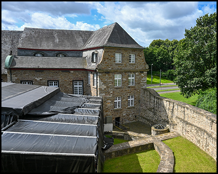 Blick von einem Turm auf den Innenhof von Schloss Broich mit einem Hauptgebäude und einer temporären Bühne davor