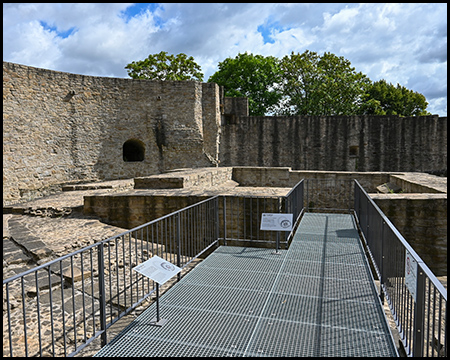 Ein Steg auf alten Mauerresten, dahinter eine Ringmauer einer Burg