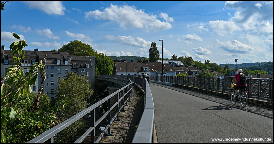 Radweg auf einer langgestreckten alten Eisenbahnbrücke. Im Hintergrund Häuserzeilen der Besiedlung unter der Brücke
