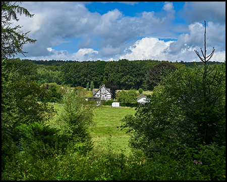 Blick über ein flaches Tal auf ein einzelstehendes Haus in einer idyllischen Landschaft