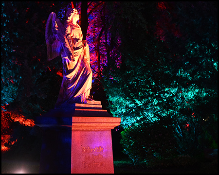 Figur auf einem Friedhof, farbig beleuchtet in der Dunkelheit