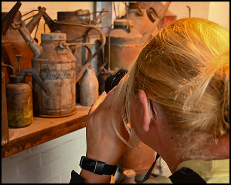 Eine Frau fotografiert Details einer Ausstellung von Öl-Behältnissen auf einem Regal